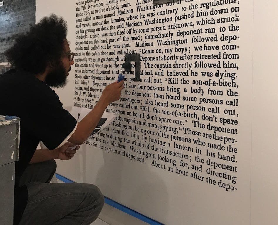A person blacks out text that has been blown-up large on a wall using with a paint roller