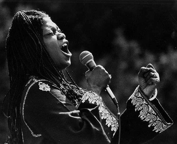 A black and white photo of a woman singing into a microphone with her eyes closed